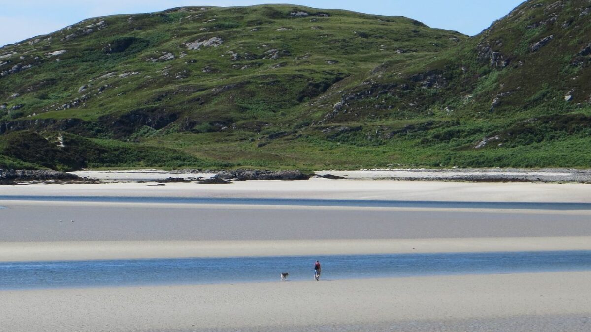 A man and his dog stroll through Silver Sands of Morar