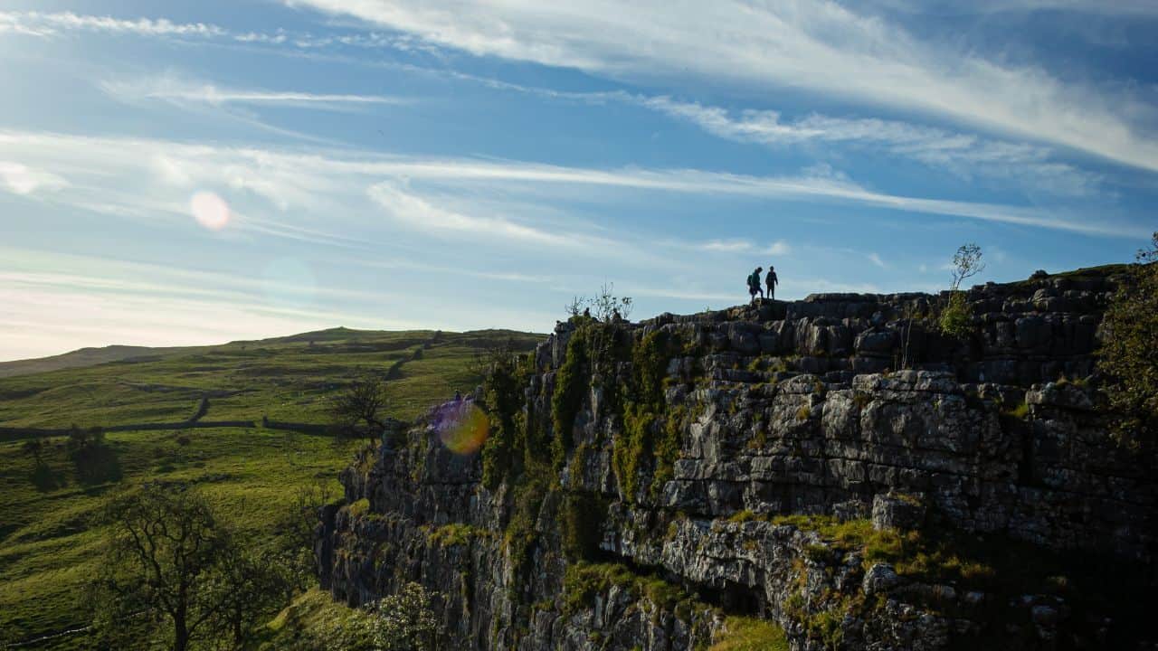 Two campers at the top of Malham Cove on a bright day