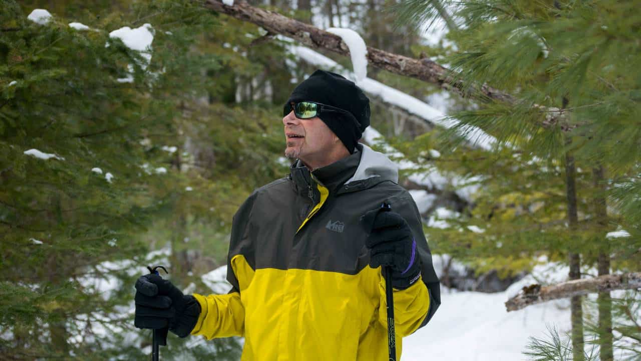 An outdoor enthusiast walking in a snowy forest while wearing a REI jacket