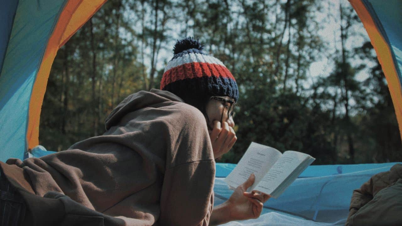 Camper wearing a hat and reading a book in her tent