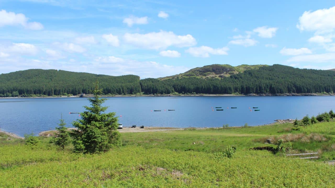 View of Loch Doon with green hills in the back and boats in the lake