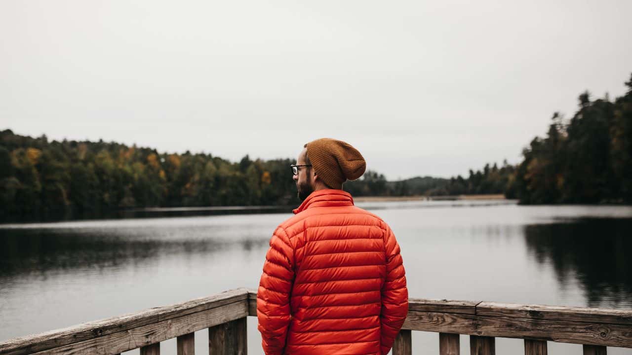 A man wearing a bright red jacket looking at the lake