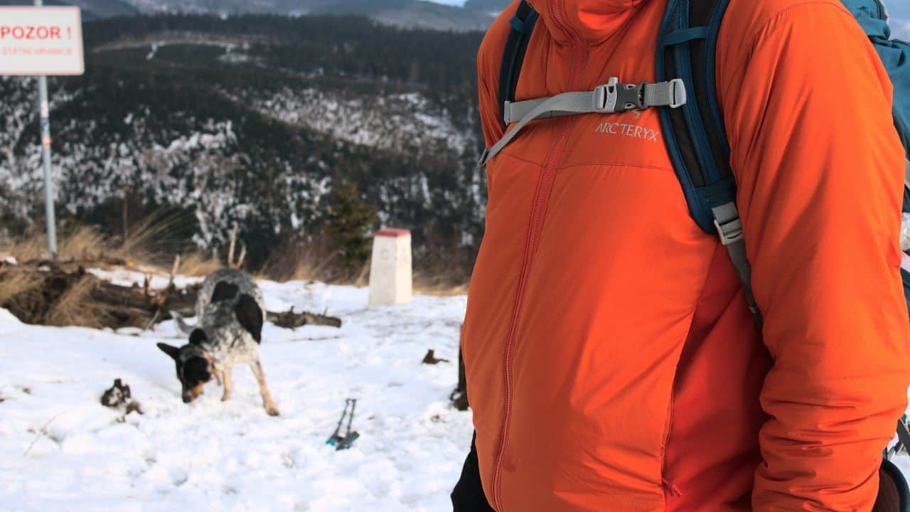 A man wearing an orange Arc'teryx jacket while hiking through snow