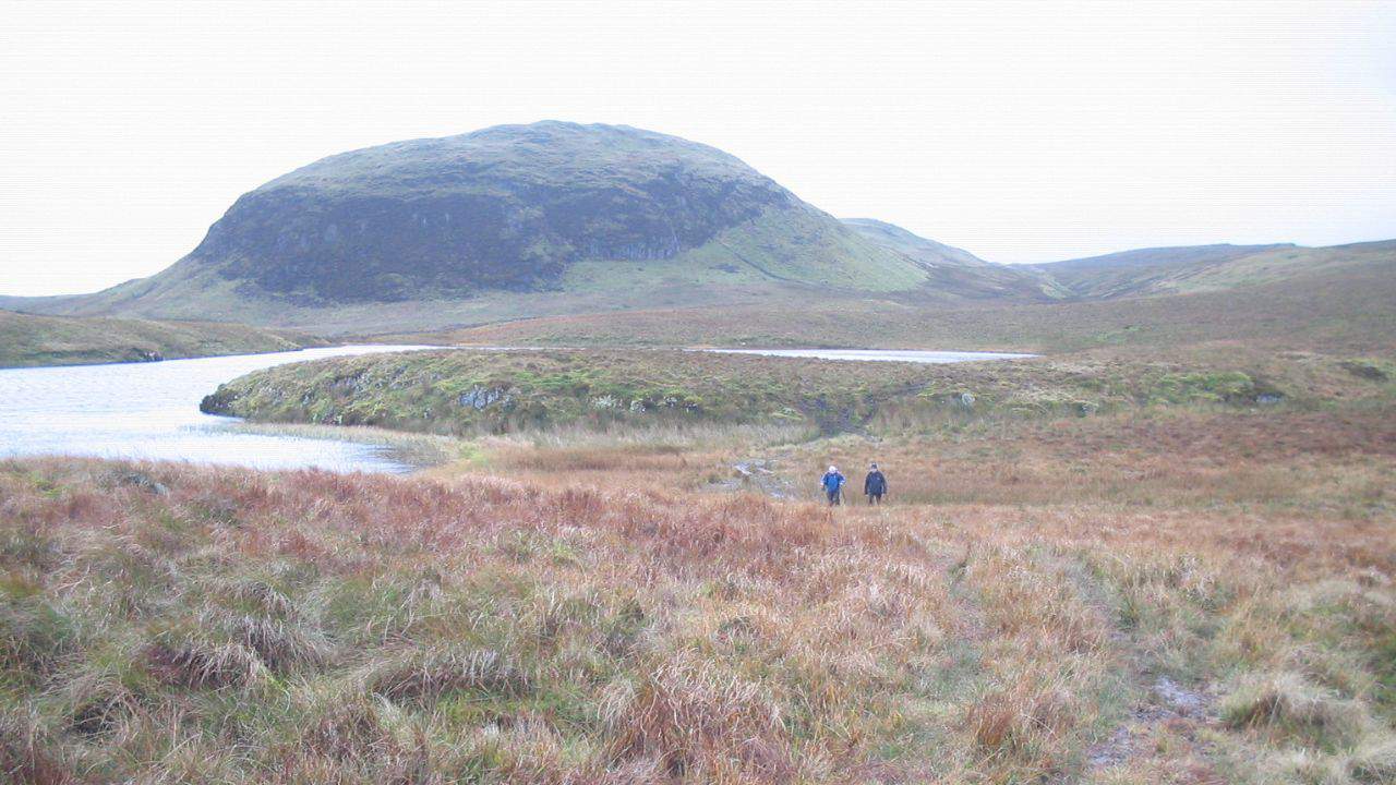 Two hikers walking next to Lily Loch with Duncolm in the back