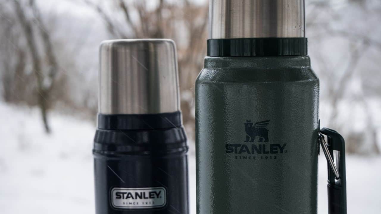 A green and a black Stanley bottles in snowy outdoors 